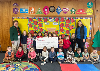 A classroom of smiling school children holding a check from IC Credit Union