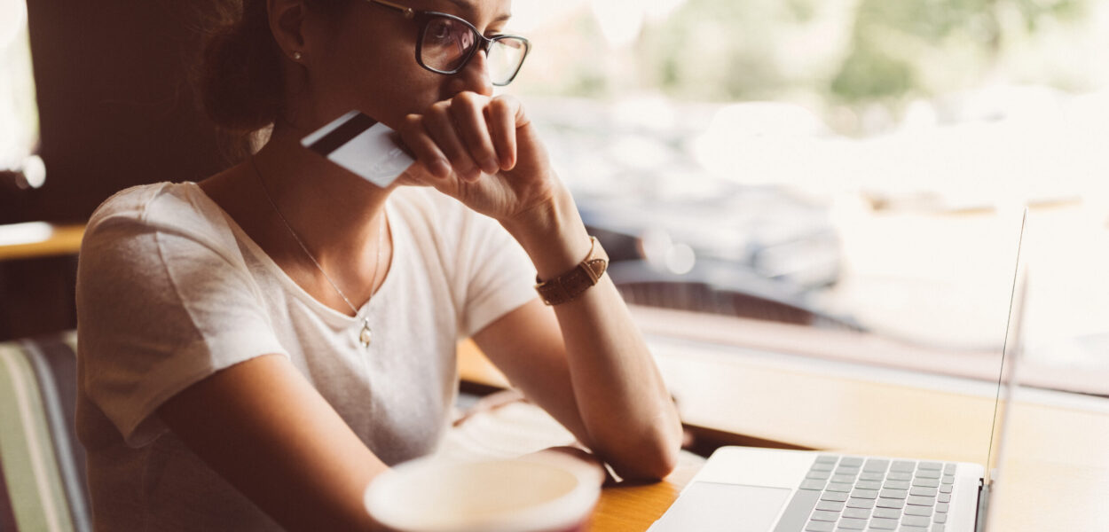 Woman victim of credt card fraud A person sitting on their laptop holding either a credit or debit card, prepared to make an online purchase
