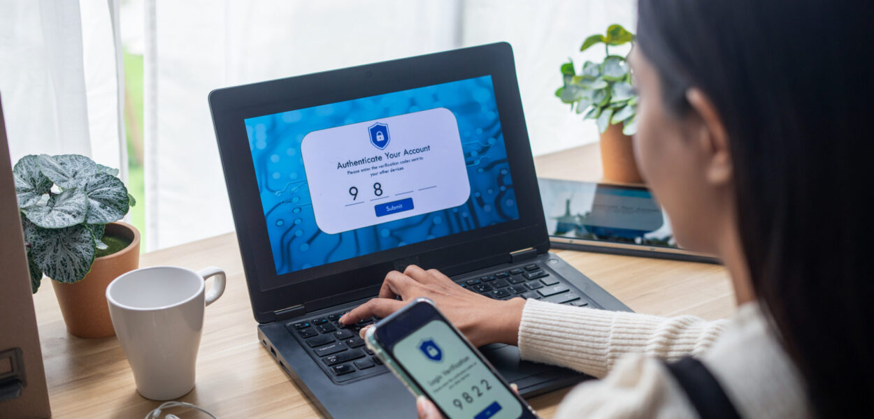 GettyImages-1788265199 (1) A person using their phone to authenticate their account on their laptop