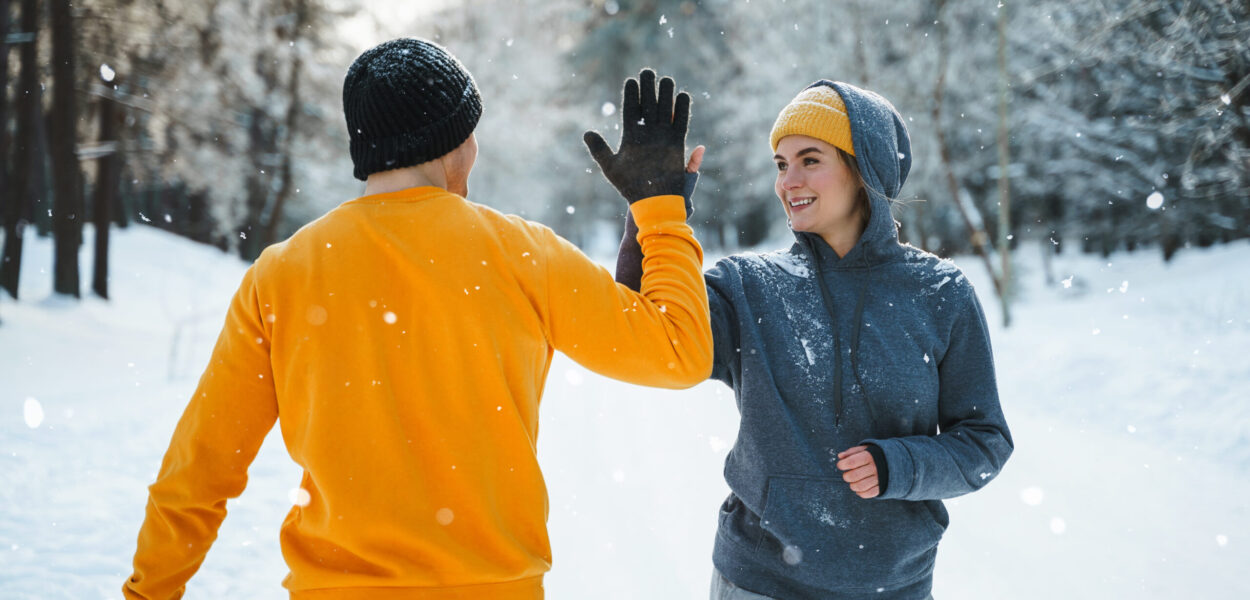 Two joggers greeting each other with a high five gesture during winter workout Two joggers greeting each other with a high five gesture during winter workout outside