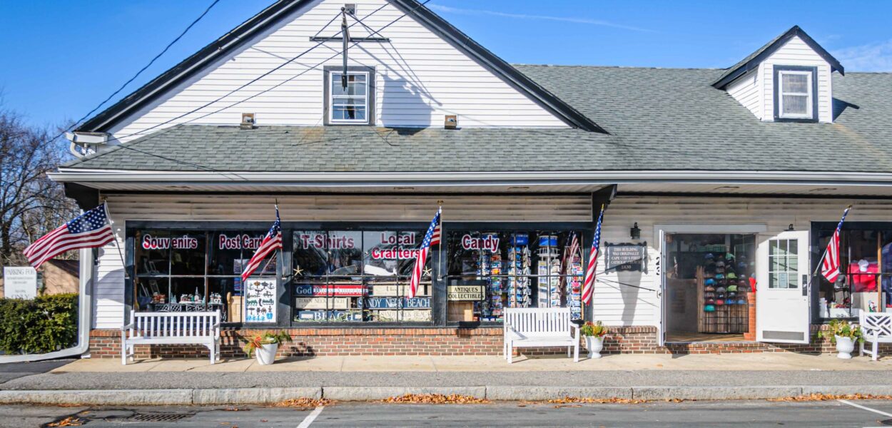 Sandwich, Massachusetts, USA-December 8, 2024- White benches rest on the sidewalk beneath a row of flags outside the Sandwich Emporium, part of a row of small, unique shops on Jarvis Street. This building, built 1830, was Cape Cod's first Catholic Church.