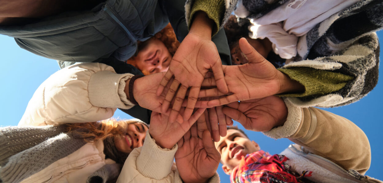 Group of young students joining hands forming a star shape, low angle view