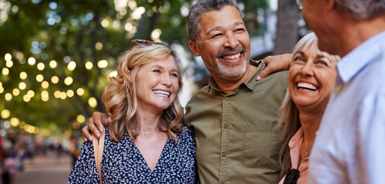 Mature women and men laughing together Group of happy senior friends sharing a moment outdoor while embrace. Older men and laughing women chatting together during a walk. Close up face of cheerful retirees enjoying time in a lively city street.