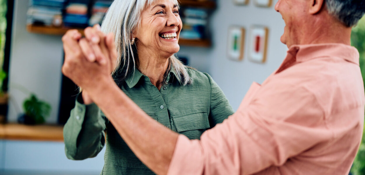 Carefree man in his 50s and woman in her 60s dancing, woman smiling towards man