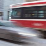 A blurry grey car speeding past a public bus in a downtown city