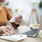 Closeup woman using calculator and holding paper bills while calculating Monthly expenses at home office.