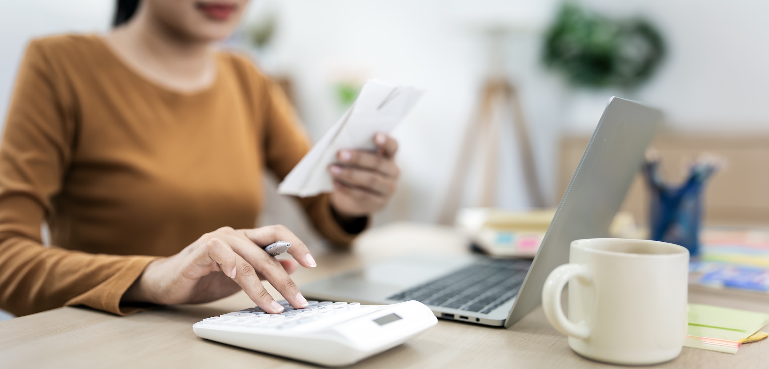 Closeup woman using calculator and holding paper bills while calculating Monthly expenses at home office.