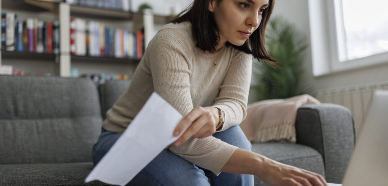 Woman reviewing financial documents while working on her laptop at home