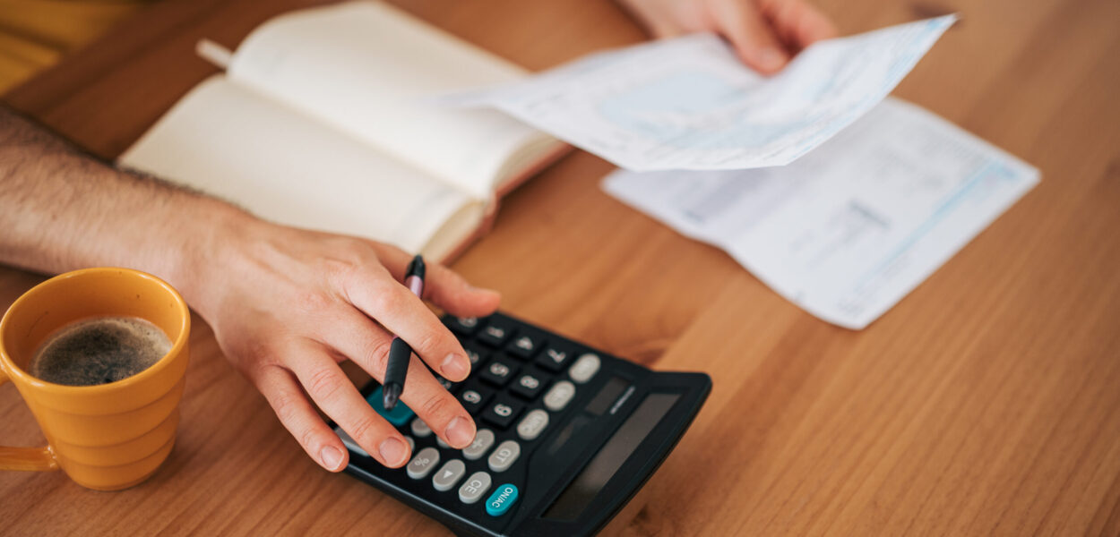 Person calculating home finances and managing budget Person's hands using a calculator, holding bills, and taking notes on a wooden table, representing personal finance management